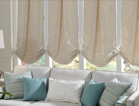 Living room with a white sofa adorned with various aqua and white pillows, situated in front of windows with beige Roman shades. Living room with a white sofa adorned with various aqua and white pillows, situated in front of windows with beige Roman shades.