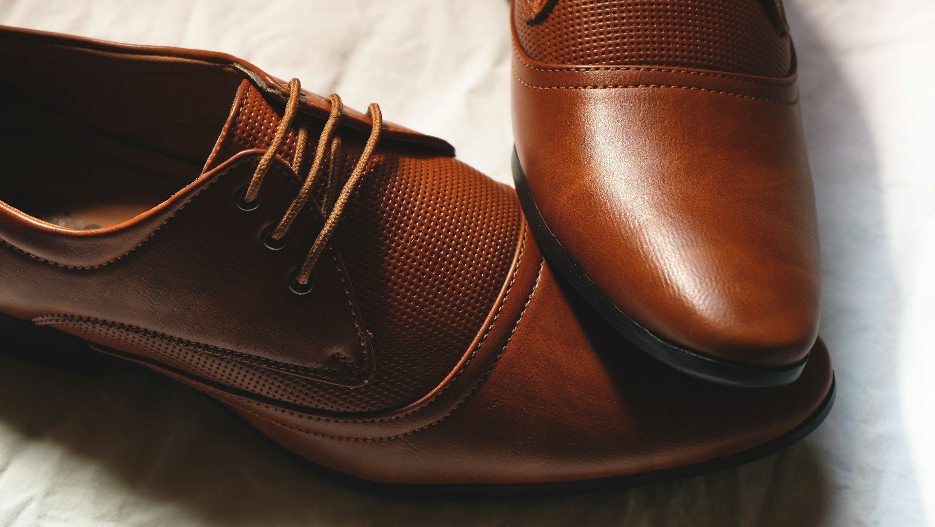 A close-up of a pair of brown leather dress shoes with laces, placed on a white surface. A close-up of a pair of brown leather dress shoes with laces, placed on a white surface.