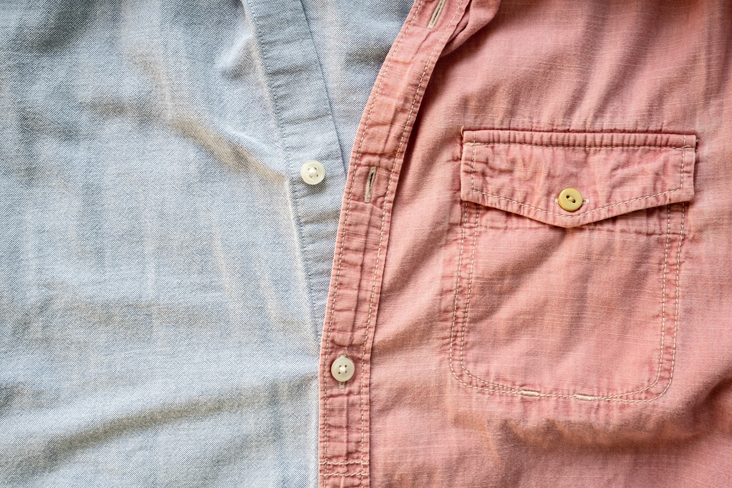 A close-up of a shirt with two colors: light blue on the left side and pink on the right, featuring a chest pocket and buttons down the middle.