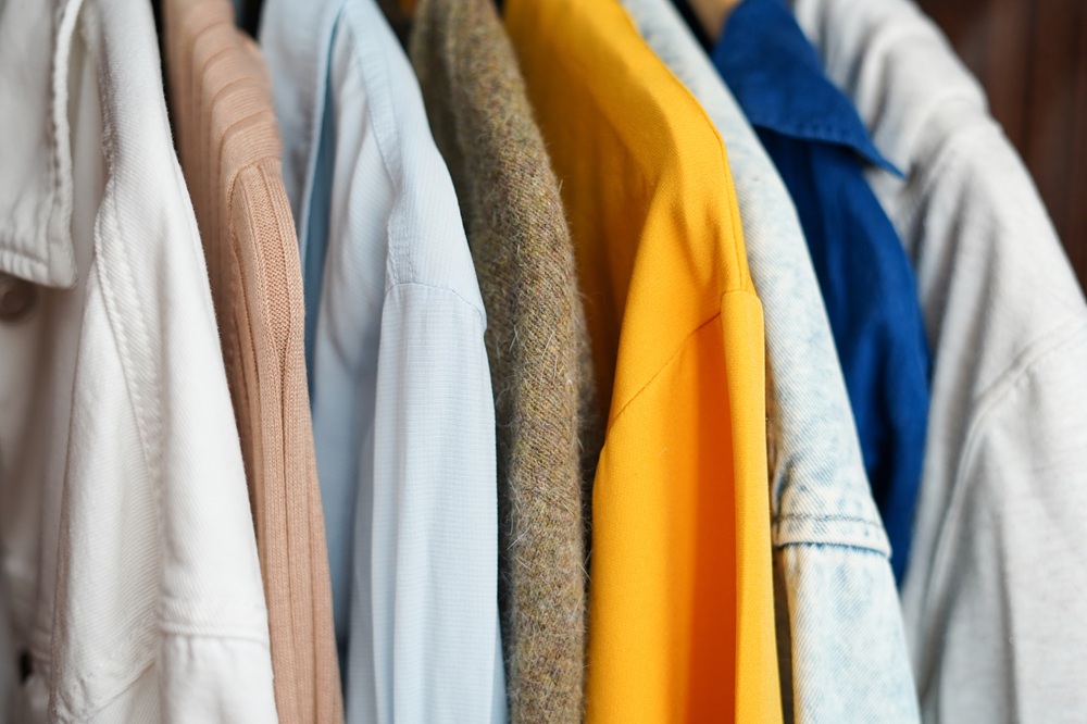 Several jackets and shirts in various colors, including white, beige, blue, yellow, and gray, are hanging on a clothing rack.