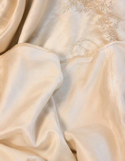 Cream-colored satin fabric with delicate floral embroidery, softly draped and gently folded.