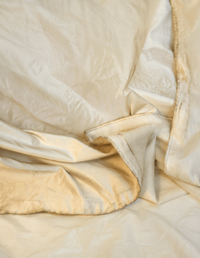 A close-up of crumpled beige satin or silk fabric, showing soft folds and slight sheen.