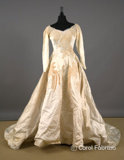 Vintage ivory satin ball gown with long sleeves, fitted bodice, and embroidered details, displayed on a black mannequin against a neutral background.