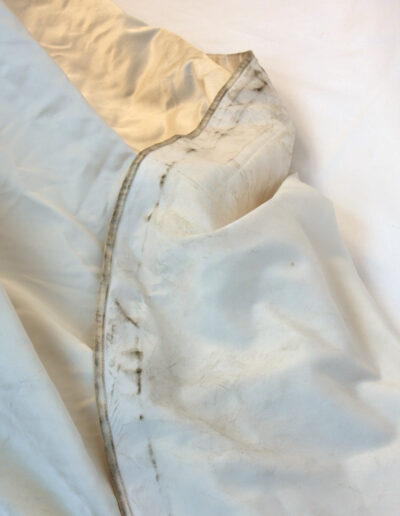 A close-up view of a white fabric with visible dirt and stains along the edges and some wrinkles throughout.