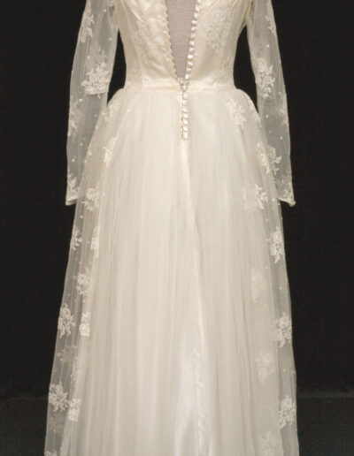 Long-sleeved vintage white wedding dress with lace overlay, buttoned back, floral embroidery, high collar, and full tulle skirt displayed on a mannequin.