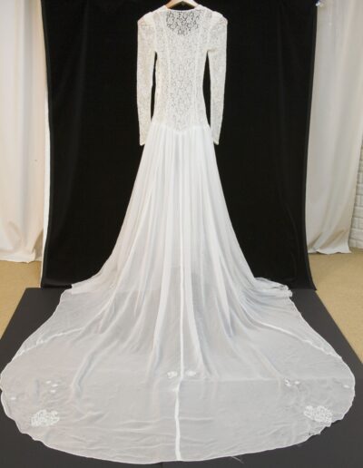 A long-sleeved, floor-length white lace wedding dress with a fitted bodice and an extended sheer train, displayed on a hanger against a black background.
