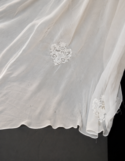 Sheer white fabric with delicate embroidered floral patterns, spread out on a dark surface.