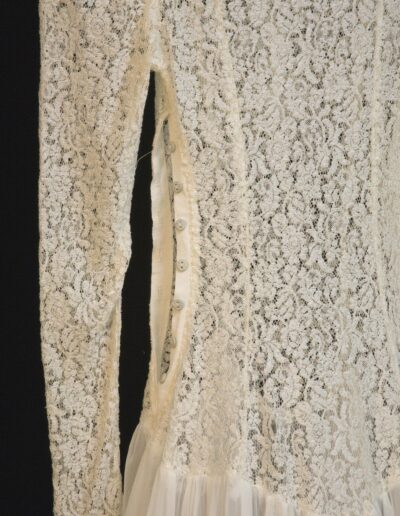 Close-up of a white lace dress showing the side seam with fabric-covered buttons and loops used as a closure.