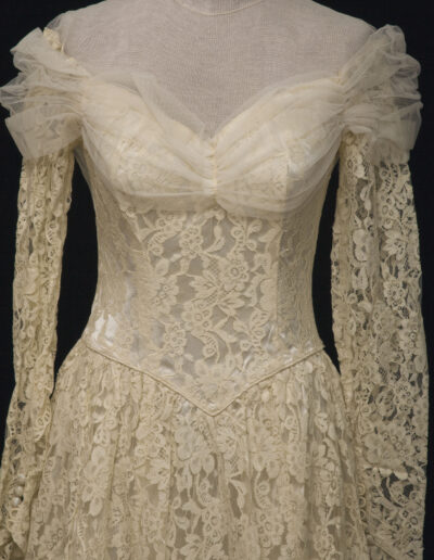 Vintage ivory lace dress with sheer off-the-shoulder neckline, fitted bodice, and long lace sleeves displayed on a mannequin.