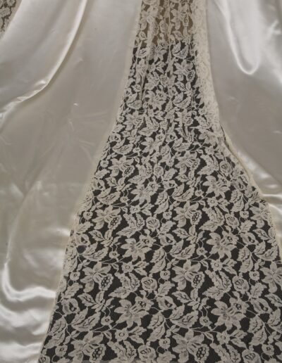 White floral lace fabric panel bordered by smooth, shiny ivory satin drapes, with intricate pattern details visible against a dark background.