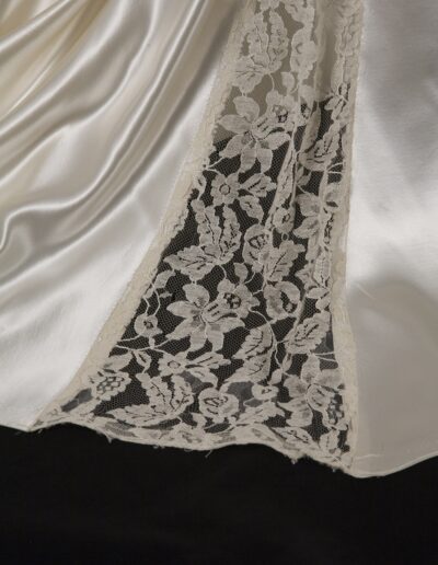Close-up of an ivory satin fabric with a floral lace inset panel, displayed on a black background.